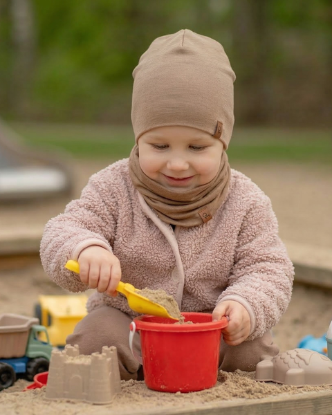 Toddler wearing beige merino wool beanie and neck gaiter while playing in sandbox, breathable kids merino wool hat and neck warmer for outdoor play, warmth, and natural temperature regulation.