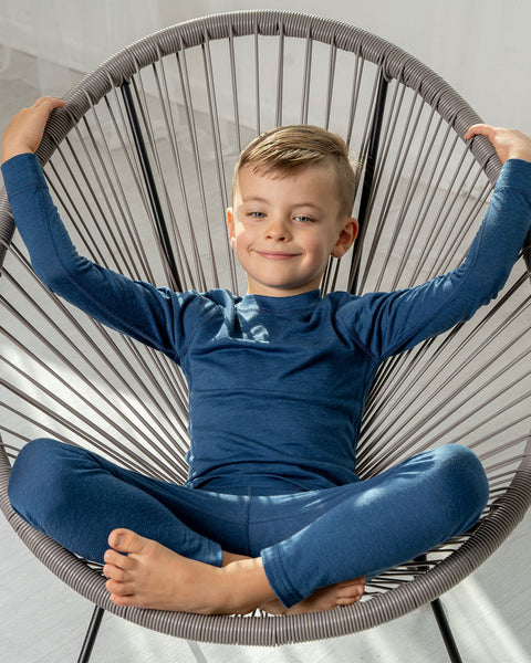 A boy wearing the menique Kids' 160 Merino Pants in Denim color. He is sitting in a lounge chair.