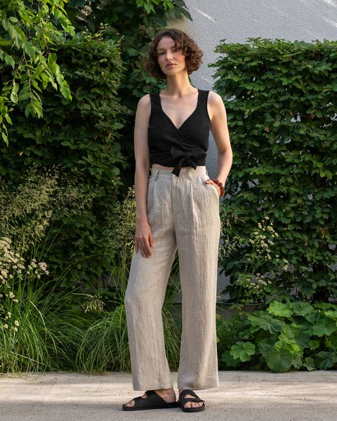 The model is wearing the ARIA linen crop top in pure black color. The photo's background is green and full of vegetation.