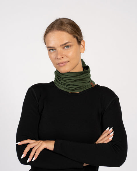 Woman wearing a dark green Merino wool neck gaiter around her neck, paired with a black top.