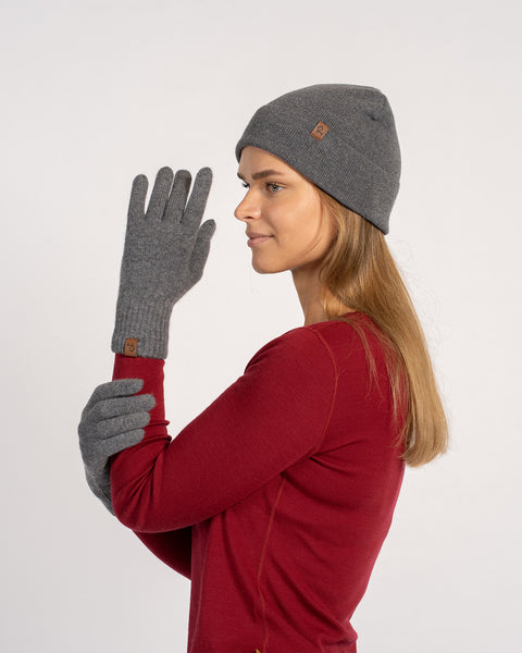 Woman in dark gray cashmere beanie and matching short gloves, side profile view, styled with a red sweater.