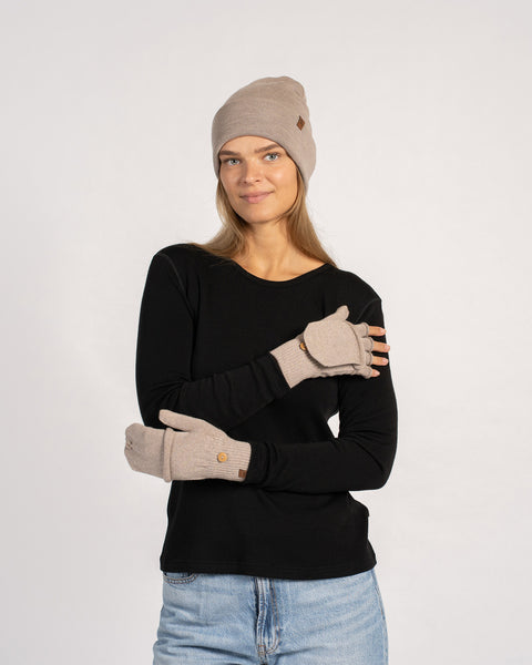 Frontal portrait of a woman smiling slightly while wearing a creamy-beige beanie and convertible mittens with flap button detail.