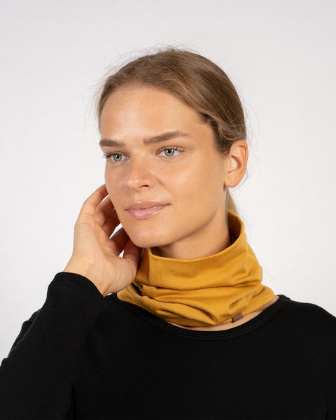 Close-up of woman with yellow Merino wool gaiter around neck, casual black top.