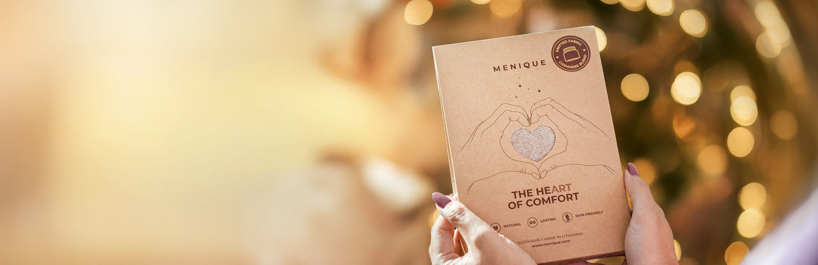 Manique product packaging held by a hand with a blurred festive background