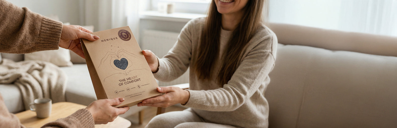 Two people holding a brown package with 'The Heart of Comfort' branding in a kitchen setting.