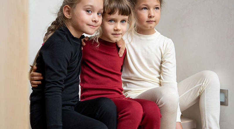 Three little girls sitting on the stair and wearing Merino wool clothing sets