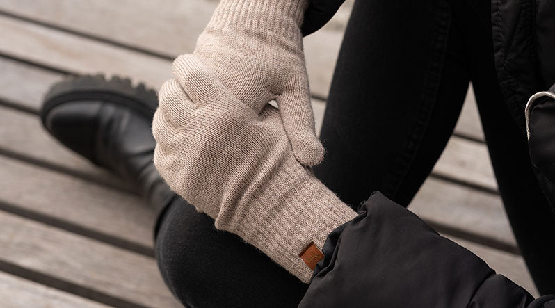 Woman outdoors holding her hands with creamy beige knitted merino wool gloves.