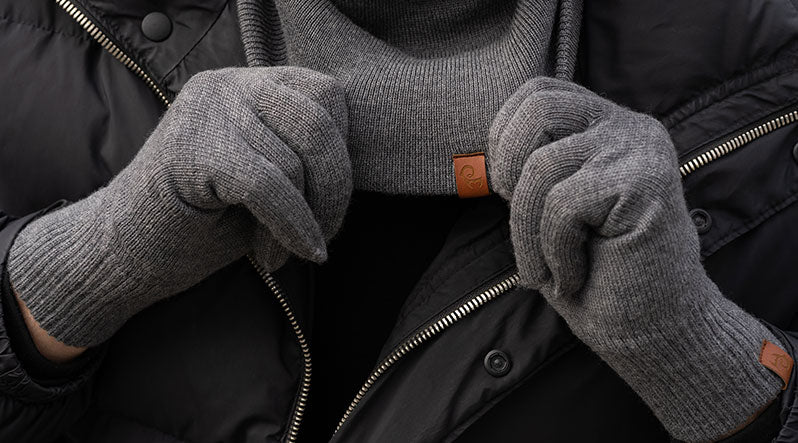 Close up of a man holding his dark gray knitted merino wool gaiter wearing dark gray knitted merino wool gloves.