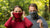 In this photo you can see man and woman standing in the forest. They are both wearing neck gaiters made from organic 100% Merino wool. Woman is wearing red color neck gaiter and Man is wearing grey one.