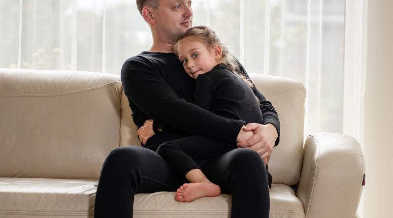 In this photo you can see dad with his daughter sitting on a sofa. They are both wearing black color matching two-piece sets made from natural 100% Merino wool.