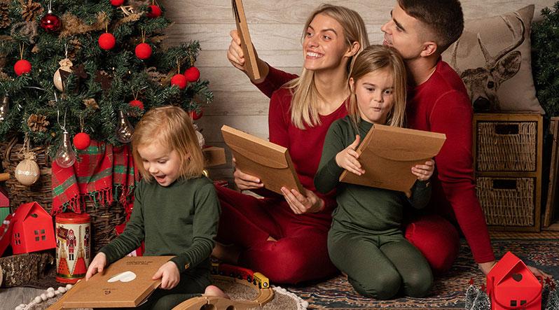 The whole family sitting near the Christmas tree. They are all wearing matching pajamas. Mom and dad are wearing royal cherry red color two-piece sets while two baby girls are wearing dark green loungewear. The clothes are made from 100% Merino wool.