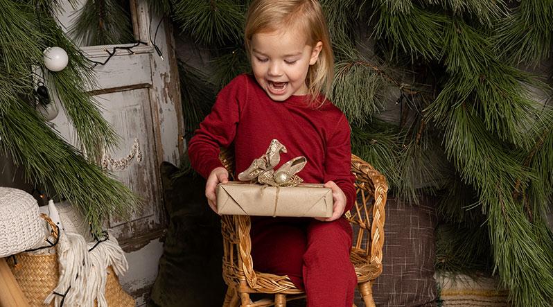 Little girl sitting on the small chair and looking with a smile at Christmas gift