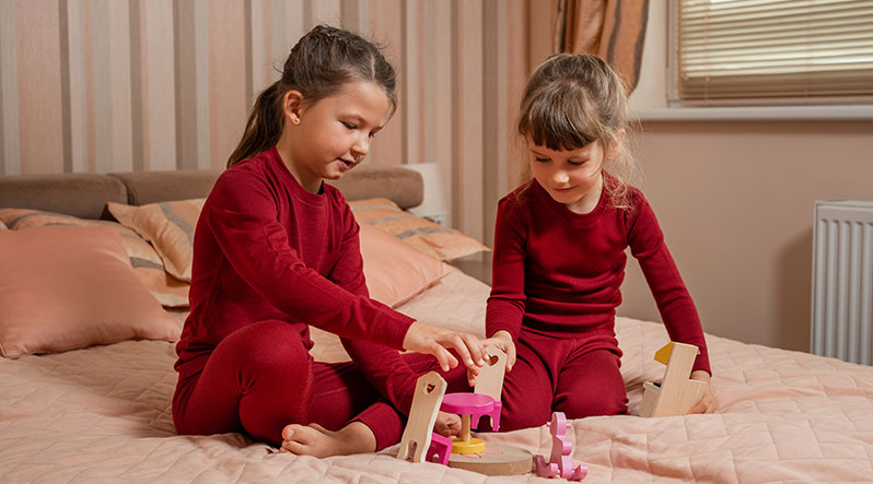 Two little girls playing on the bed with wooden toys