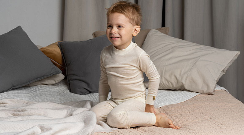 Little boy on the bed is wearing natural merino wool matching set