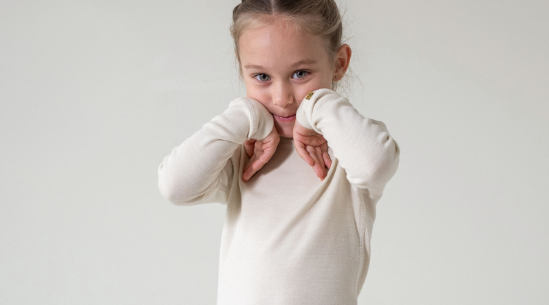 A little todler girl wearing merino wool long sleeve shirt of 250gsm merino wool fabric, in natural color.