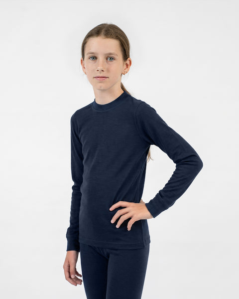 A young girl modeling a long-sleeved navy blue thermal top, standing with one hand on her hip against a white background.