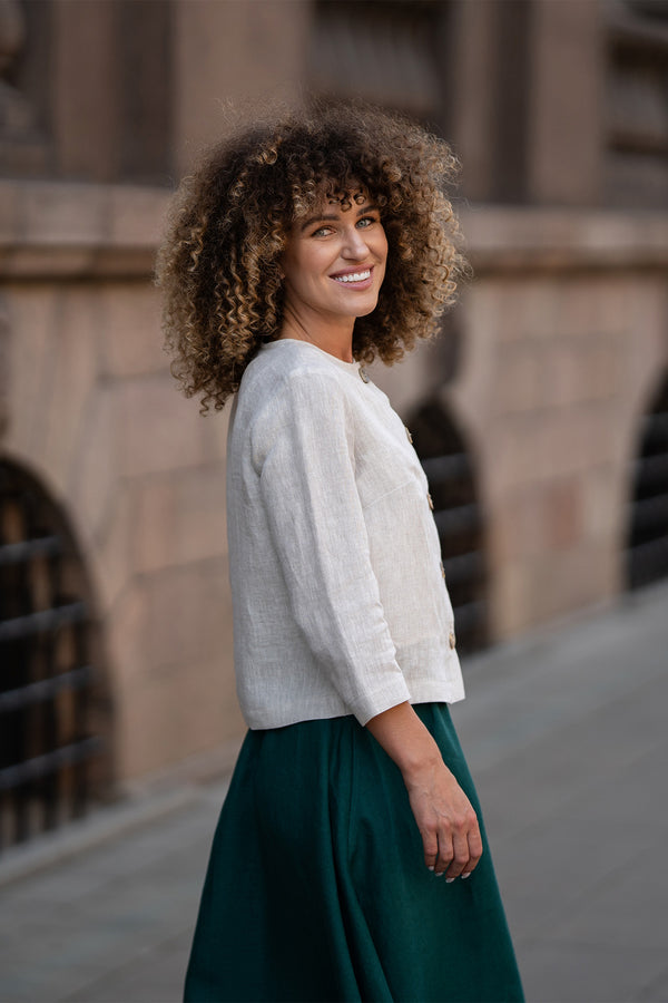 A model wearing a natural beige linen jacket Alice with buttons, featuring a relaxed fit, 3/4-length sleeves, and a minimalist design