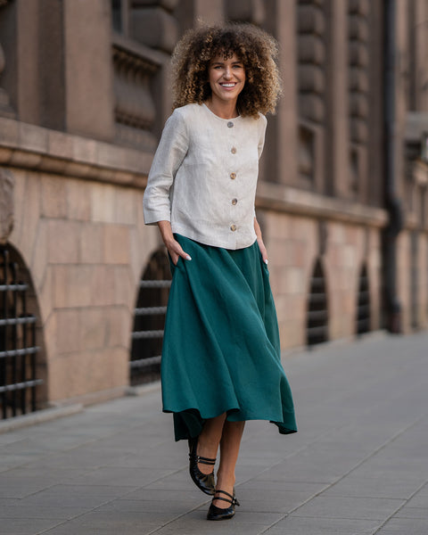 A model wearing a natural beige linen jacket Alice with buttons, featuring a relaxed fit, 3/4-length sleeves, and a minimalist design. The jacket is paired with matching dark green skirt