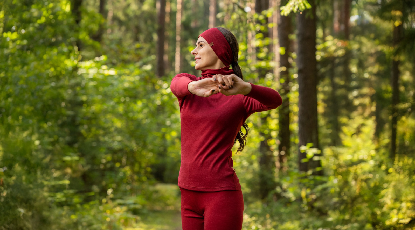 Woman stretching outdoors wearing red merino wool base layer and headband, breathable thermal activewear for hiking, running, and outdoor fitness in changing weather conditions.