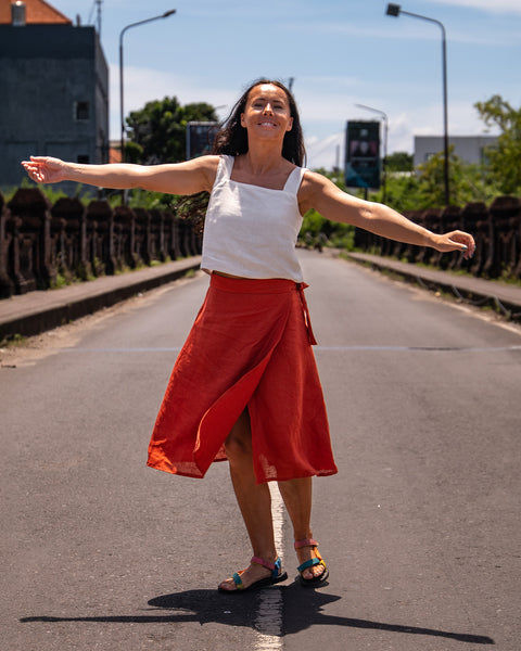 A woman wearing a white top and an orange skirt, looking up and smiling.