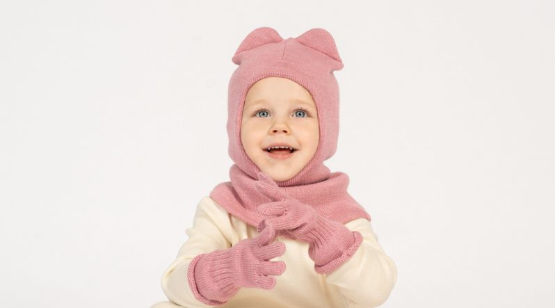 Little girl smiling and wearing dusty pink merino wool balaclava with ears and gloves