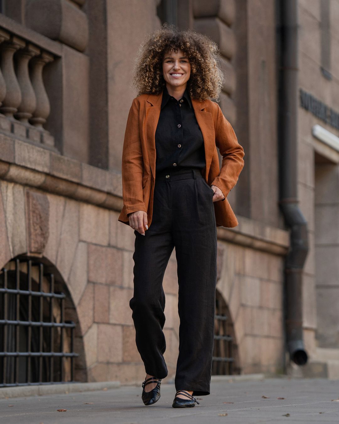 Woman in a brown coat standing in front of a stone building