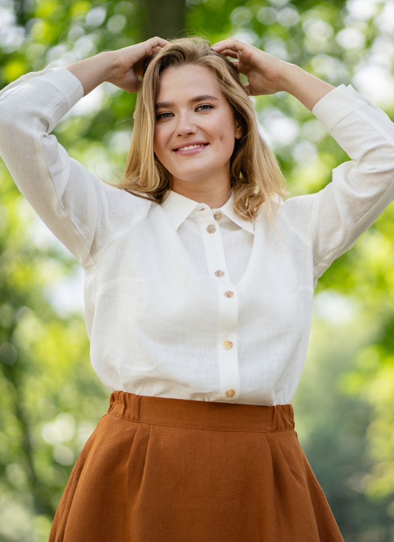 Woman wearing white linen blouse outdoors in a natural setting.