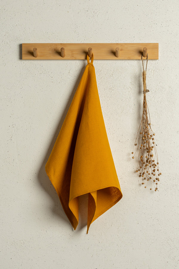 The menique linen kitchen dish towel in the color of spicy yellow hanging on a wooden rack on a wall.