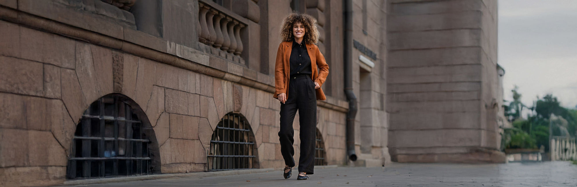 Woman in an orange jacket standing in front of a stone building