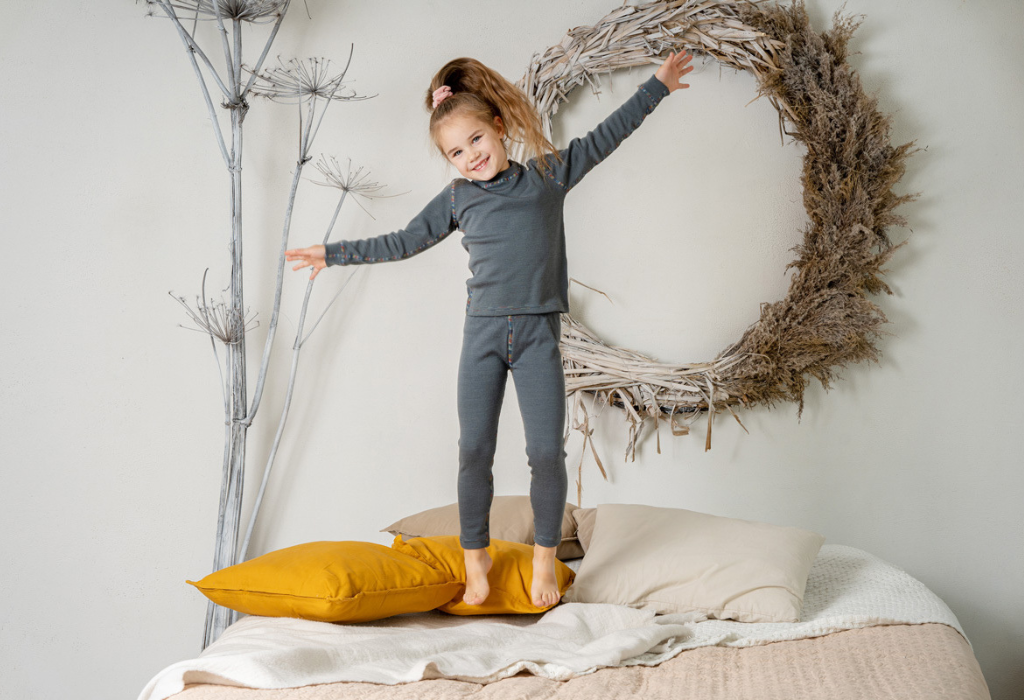 Photo of girl jumping on bed with merino wool clothing from menique