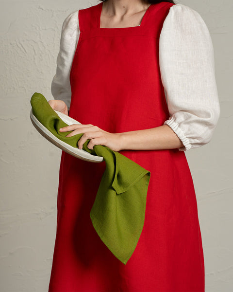 A person wearing a red apron and white blouse drying a plate with a green linen kitchen towel.