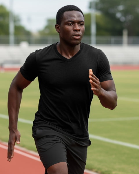 A man sprinting on a track field, wearing a fitted black V-neck T-shirt and black athletic shorts, focused on his run.
