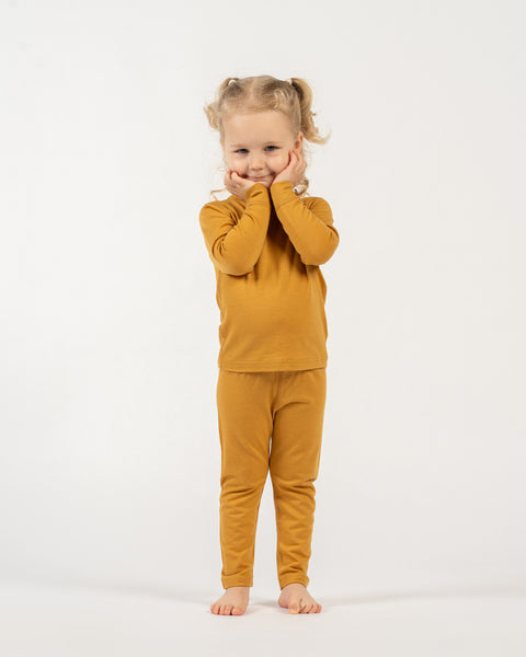 Young girl wearing a menique merino wool yellow long sleeve and bottom set on a white background