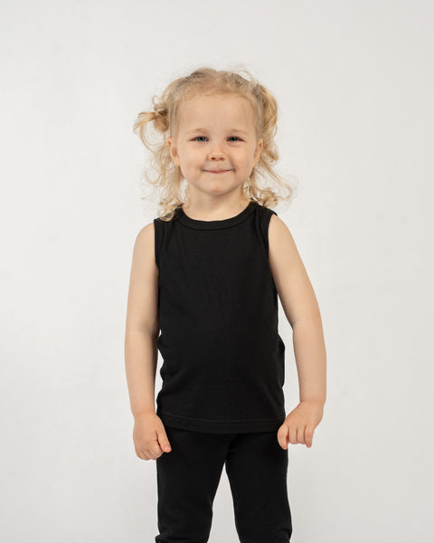 Young child wearing a black menique sleeveless top made from merino wool and matching black pants on a white background