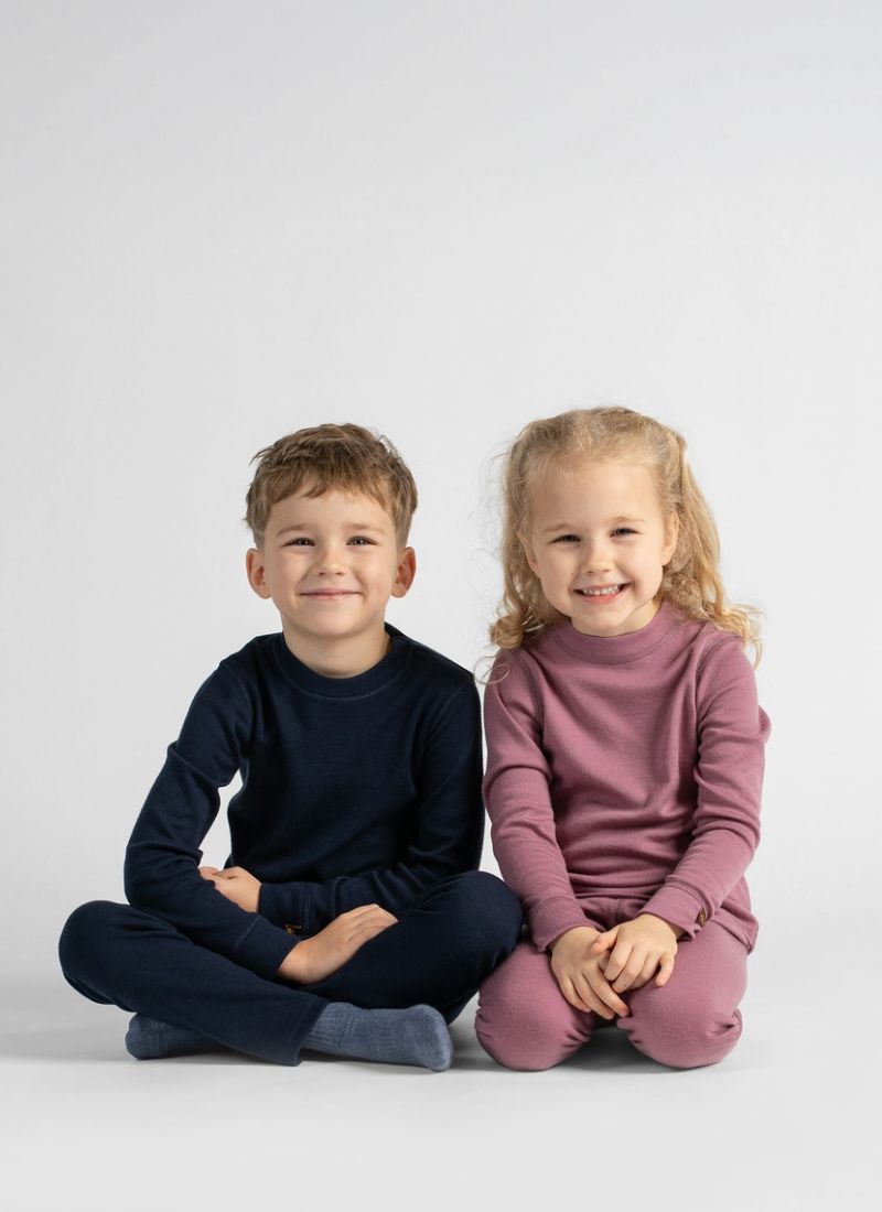 A young boy in navy thermal wear and a young girl in berry-pink thermal wear sitting side-by-side on the floor smiling.