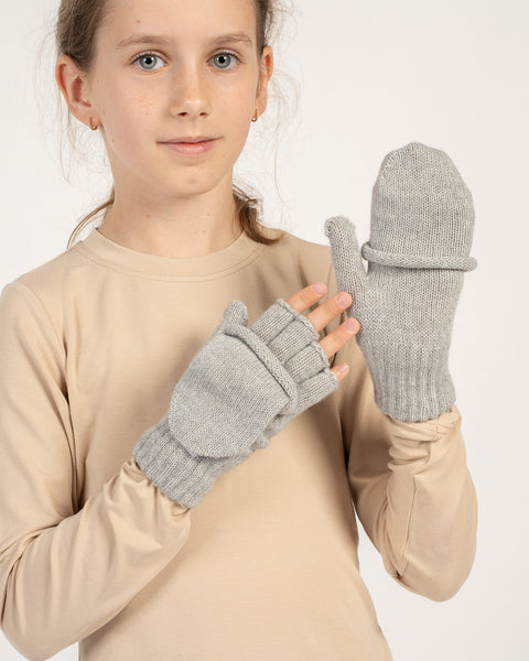 Girl wearing light gray knitted convertible mittens, one flap closed as a mitten, the other open to show fingerless style.