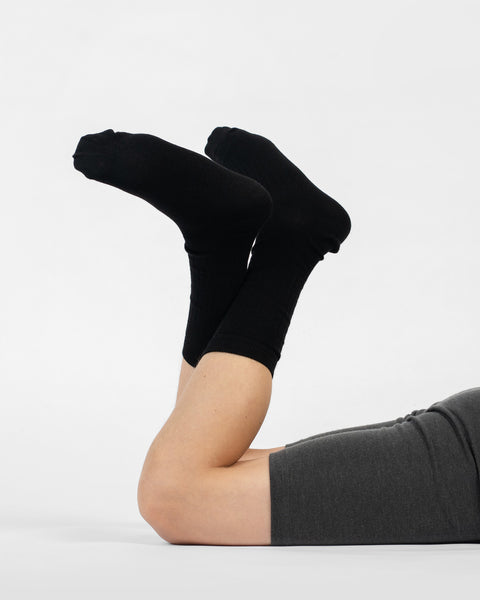 A person lying on their stomach with their lower legs raised, modeling black ribbed merino crew socks.
