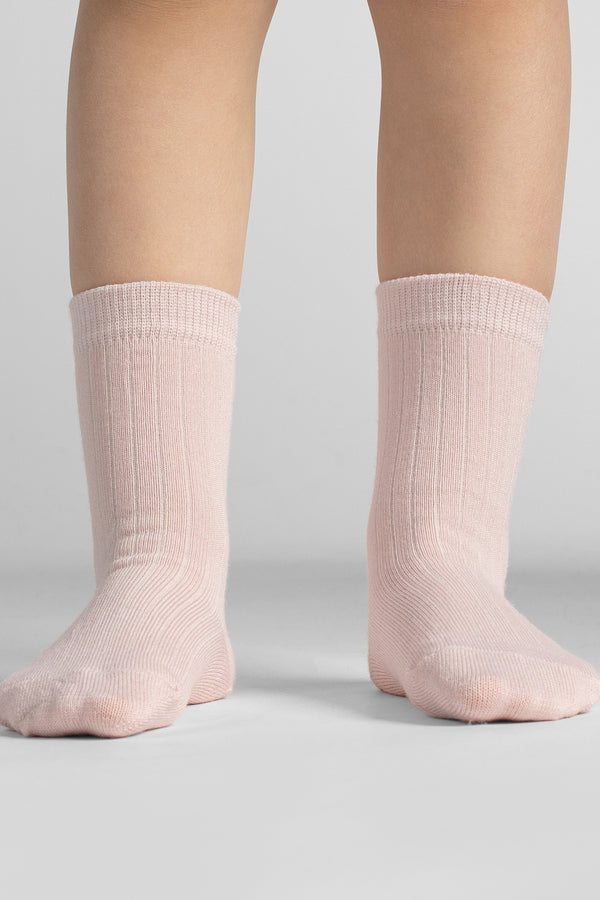 Close-up front view of bare legs standing straight, wearing ribbed light pink crew socks against a neutral background.