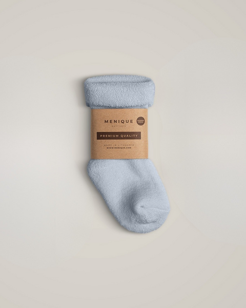 A single light blue fuzzy baby sock with a folded cuff, wrapped in a brown cardboard label that reads "MENIQUE" and "Premium Quality", placed against a plain light gray background.
