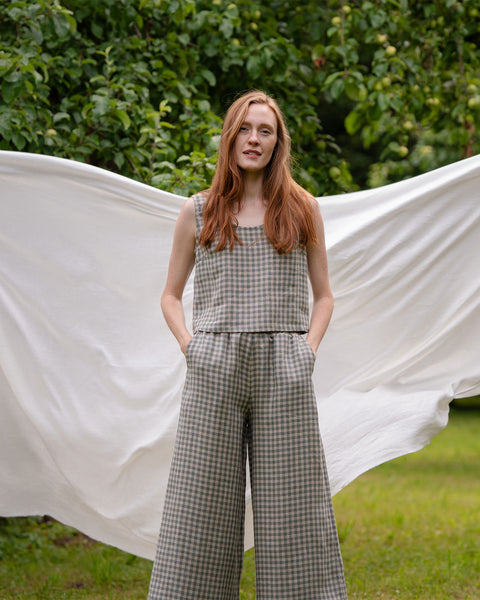 The model is facing the camera, wearing the matching set of ANA crop top and Lana culottes. She has both of her hands in the side pockets of the pants. Behind her is a white sheet visible.