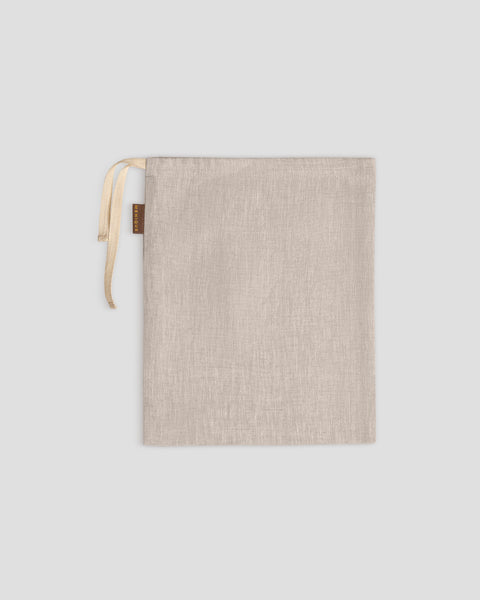 A menique organizing bag lies flat on a light gray background. Its drawstrings are gathered at the top left, next to a small brown tag.