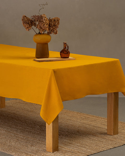 Vibrant yellow linen tablecloth with floral centerpiece for a warm, inviting dining room setup.