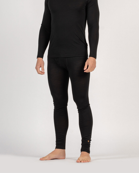 A person from the neck down standing barefoot against a white background, wearing a fitted, black long-sleeved thermal top and matching thermal leggings with a front fly. Their arms are relaxed at their sides.