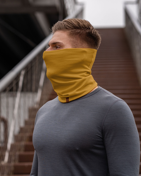 A man with short, blond hair is shown in a profile view, his gaze directed towards the left, as if lost in thought. He's wearing a vibrant spicy yellow neck gaiter that contrasts against his gray long-sleeved shirt. 
