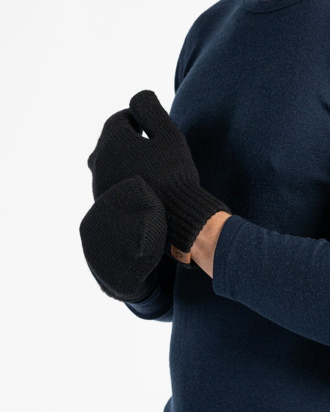 A person wearing a dark blue long-sleeved shirt and black menique mittens. The person is holding their hands together.