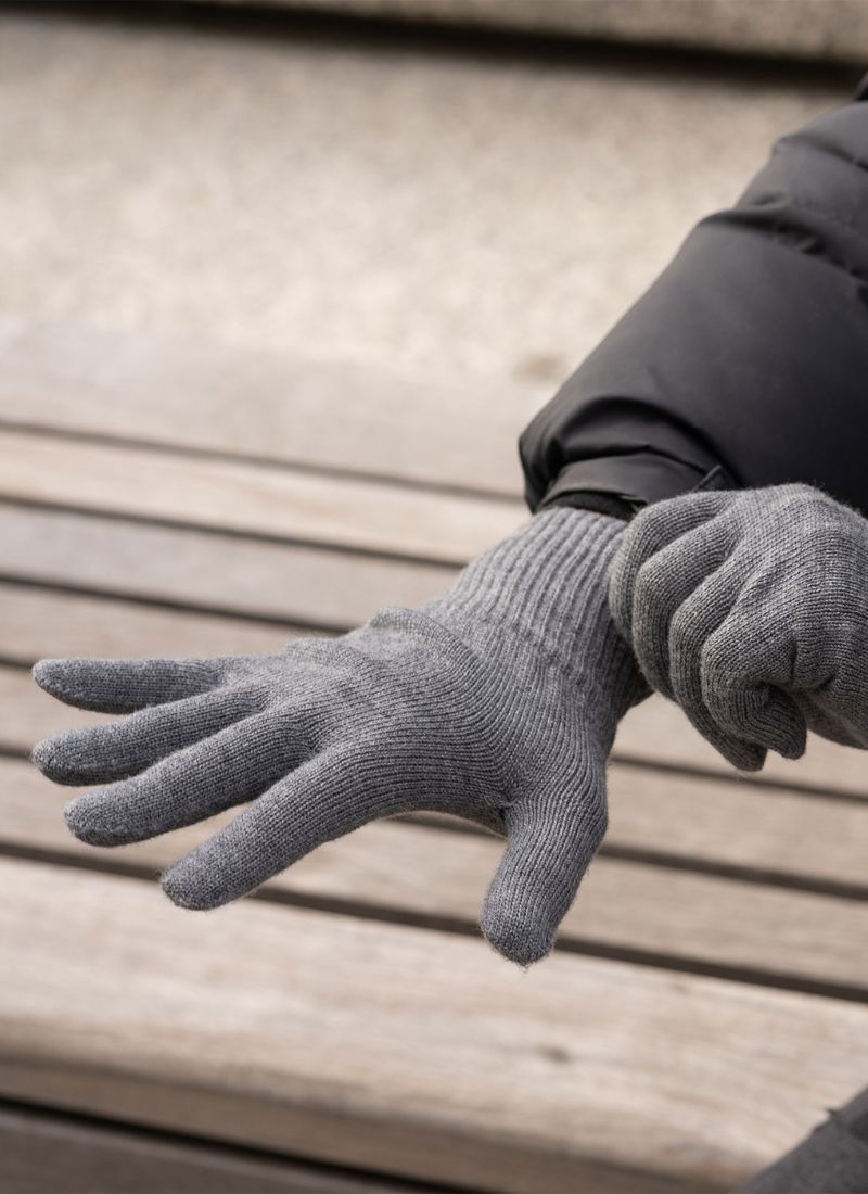 A person pulling up a merino wool glove in dark gray color.