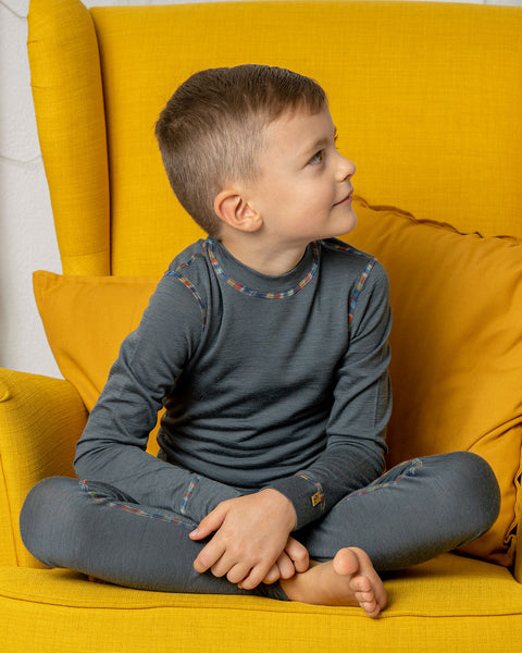 A boy sitting in a yellow armchair, looking to the side, wearing the menique long sleeve merino top in perfect gray color with matching pants.