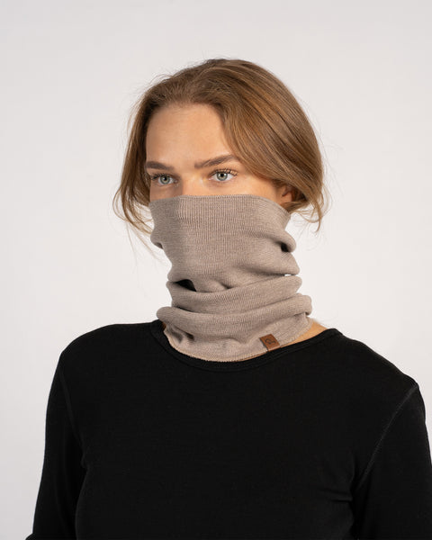 Woman wearing a creamy beige knitted Merino wool gaiter pulled up over the nose and mouth.