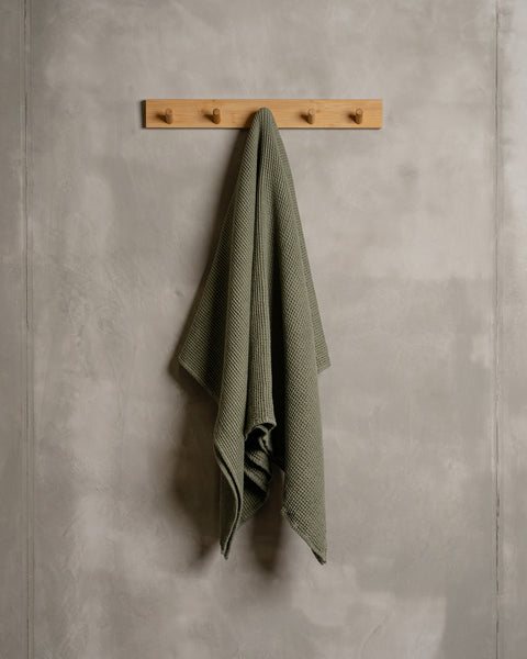 A linen &amp; cotton waffle body towel in stone green color hanging on a wooden rack.