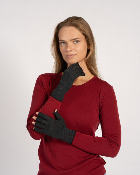 Frontal image of a woman in a red top wearing dark-gray fingerless gloves, one hand near her chin and the other across her torso.